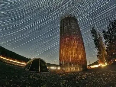 A tent pitched beside the historic silo at The Glendale Farm under circular star trails, Chimacum, Washington